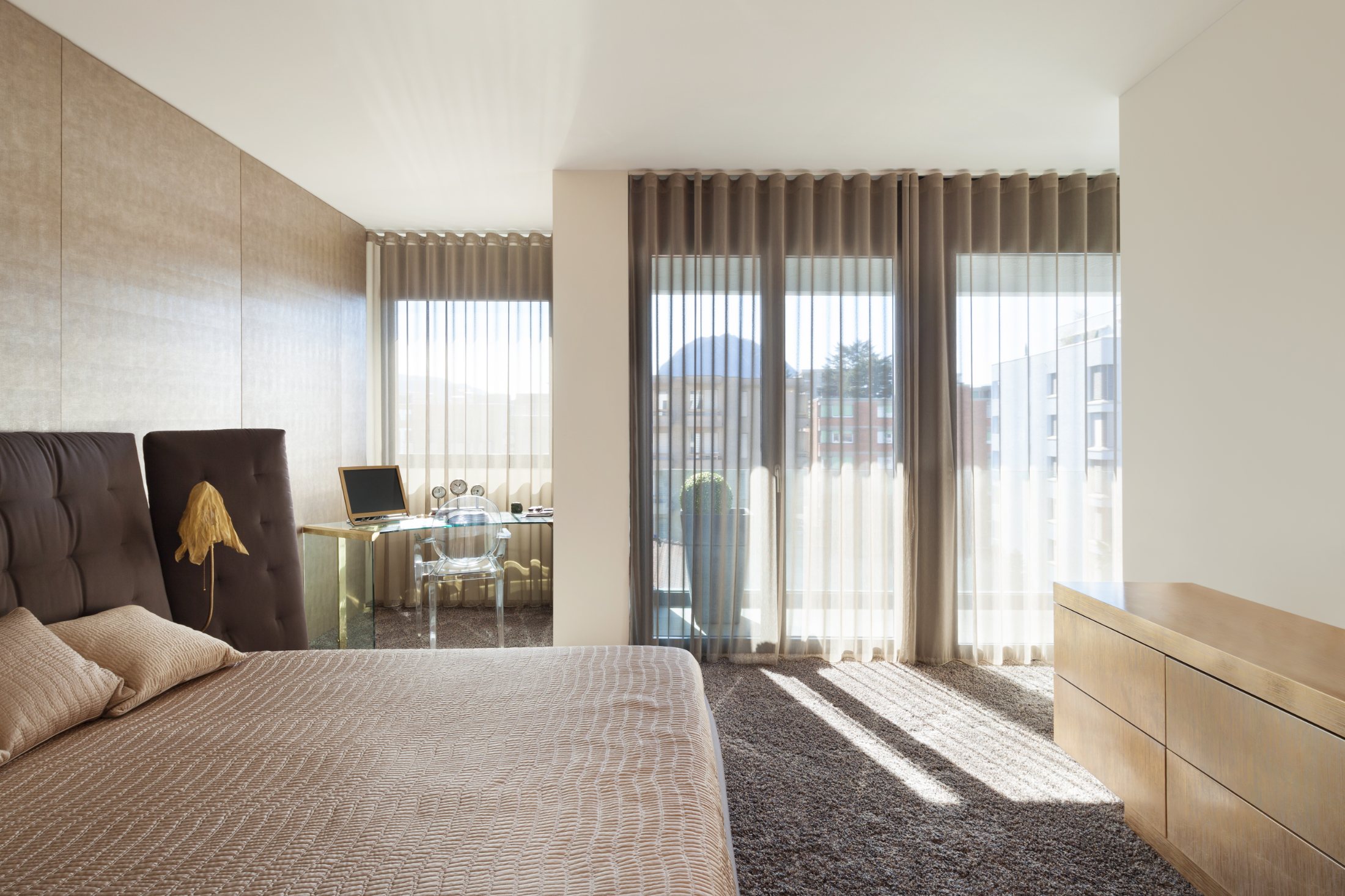 Floor-to-ceiling sheer curtains filtering soft daylight in a neutral bedroom